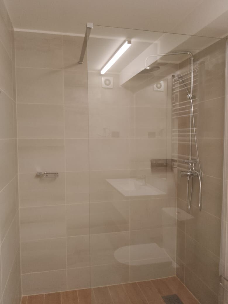 Baño con ducha de vidrio y revestimiento claro